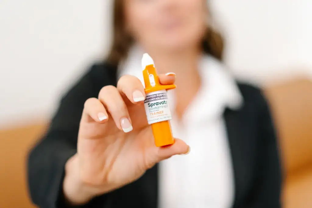 A healthcare professional holding a Spravato (esketamine) nasal spray trainer, demonstrating its use for educational or informational purposes. The focus is on the device, with the professional's face softly blurred in the background.
