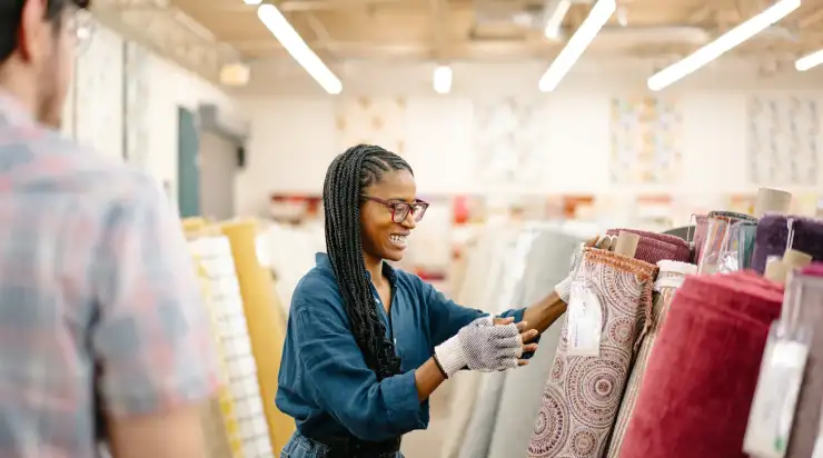 Smiling woman with long braids wearing gloves and selecting fabric rolls in a well-lit store, highlighting small business branding in action.