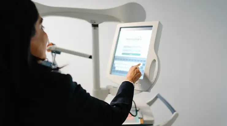 A woman uses a touchscreen interface on a TMS machine in a modern clinical setting, highlighting advanced technology in healthcare environments.