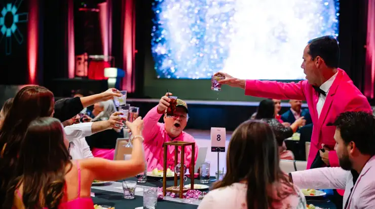 Guests wearing pink and white outfits raising glasses in a celebratory toast around a decorated table at a StatLab award ceremony in Dallas.