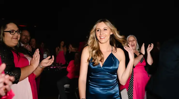 A woman in a blue satin dress smiles while walking through a crowd applauding her at an awards ceremony in Dallas, Texas.