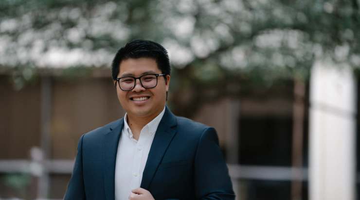 Professional traditional headshot of a man in a navy suit and white shirt, smiling outdoors with a softly blurred background—ideal for corporate profiles, LinkedIn, and company websites.