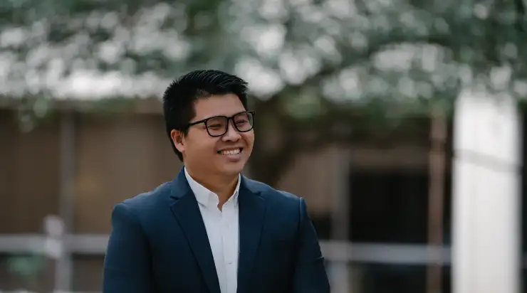 Branding photo of a man in a navy suit and glasses, smiling and looking off-camera outdoors—this relaxed, approachable image style is ideal for business websites, social media, and marketing materials, going beyond a traditional headshot to showcase personality and brand story.